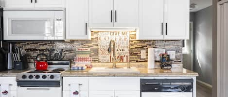A modern kitchen with white cabinets, a red kettle, and a backsplash with a motivational quote.