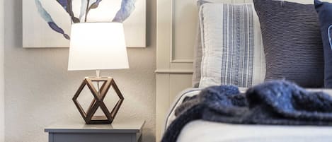 A neatly made bed with a blue blanket, a bedside lamp, and a framed artwork on the wall.