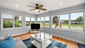 A spacious living room with large windows, a ceiling fan, and a flat-screen TV. - Beautiful Home in Ocean Pines with Water Access for SUP's and Canoes (Ocean Pines)