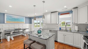A modern kitchen with white cabinets, a marble island, and a dining area with a bench. - Beautiful Home in Ocean Pines with Water Access for SUP's and Canoes (Ocean Pines)