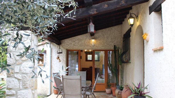 An outdoor patio with stone walls, a wooden table and chairs, and potted plants.