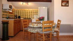 A compact kitchen with a dining area, featuring a tiled backsplash, wooden cabinets, and a small island with a microwave.