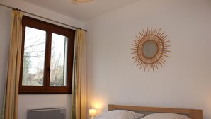 A bedroom with a bed, a window with curtains, a radiator, and a wall-mounted sun decoration.