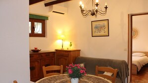 A cozy dining area with a round table, chairs, a vase of flowers, a chandelier, and a painting on the wall.