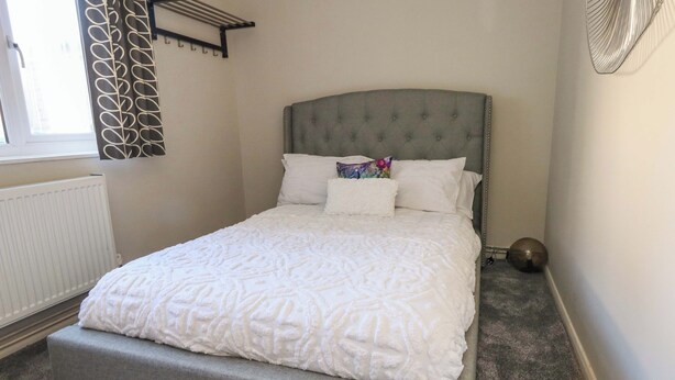 A neatly made bed with a grey headboard, white bedding, and a radiator below. - Lily's Pad (Portland)