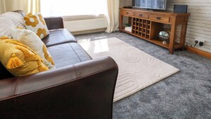 A living room with a brown leather sofa, a white rug, a wooden TV stand with a flat-screen TV, and a brick-patterned wall. - Lily's Pad (Portland)