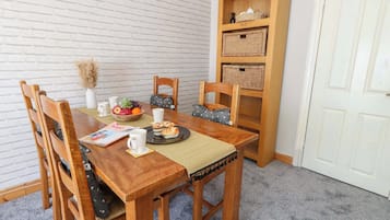 A dining area with a wooden table, chairs, a white brick wall, and a bookshelf.