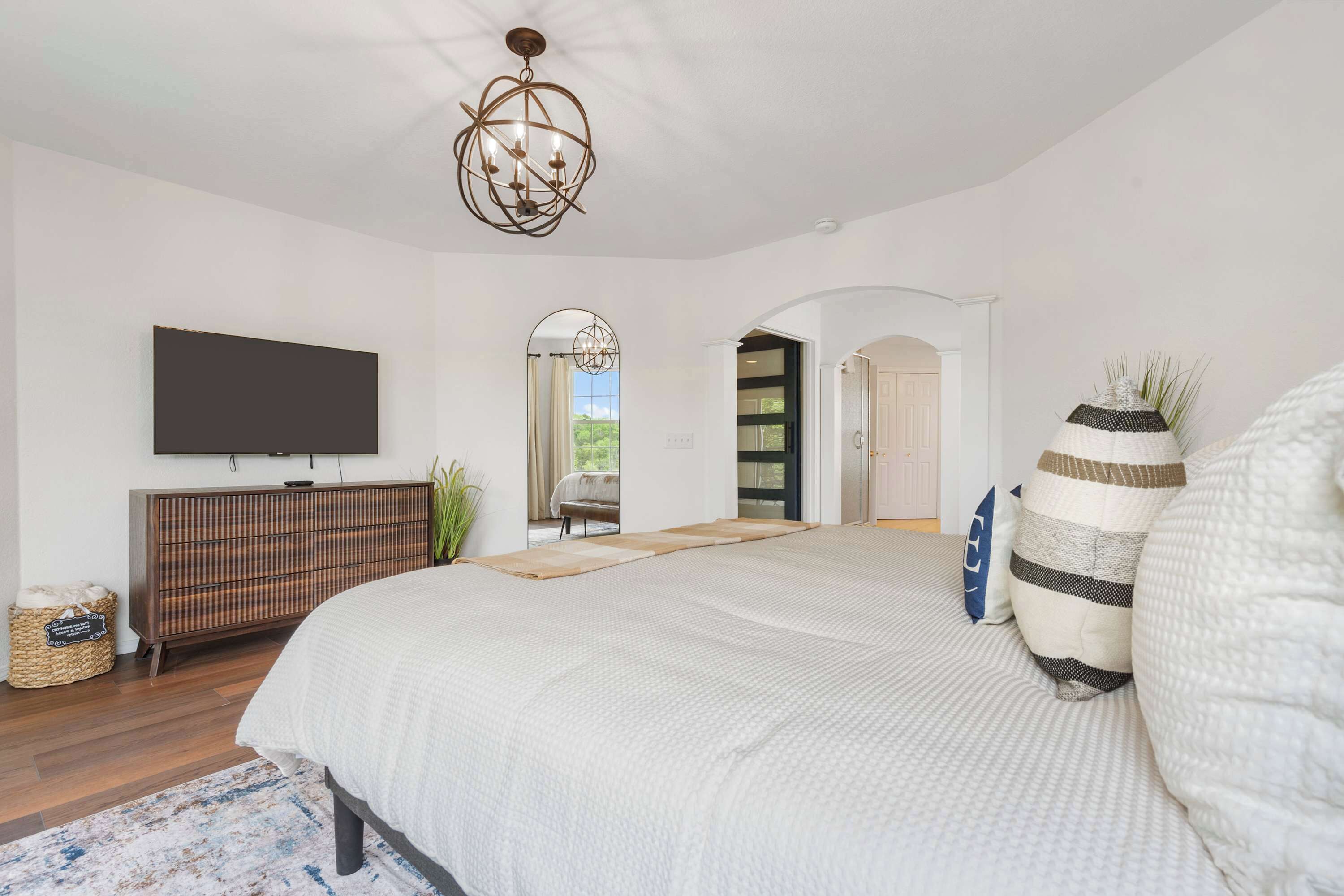A bedroom with a large bed, a television on the wall, a wooden cabinet, and a view of the outdoors.