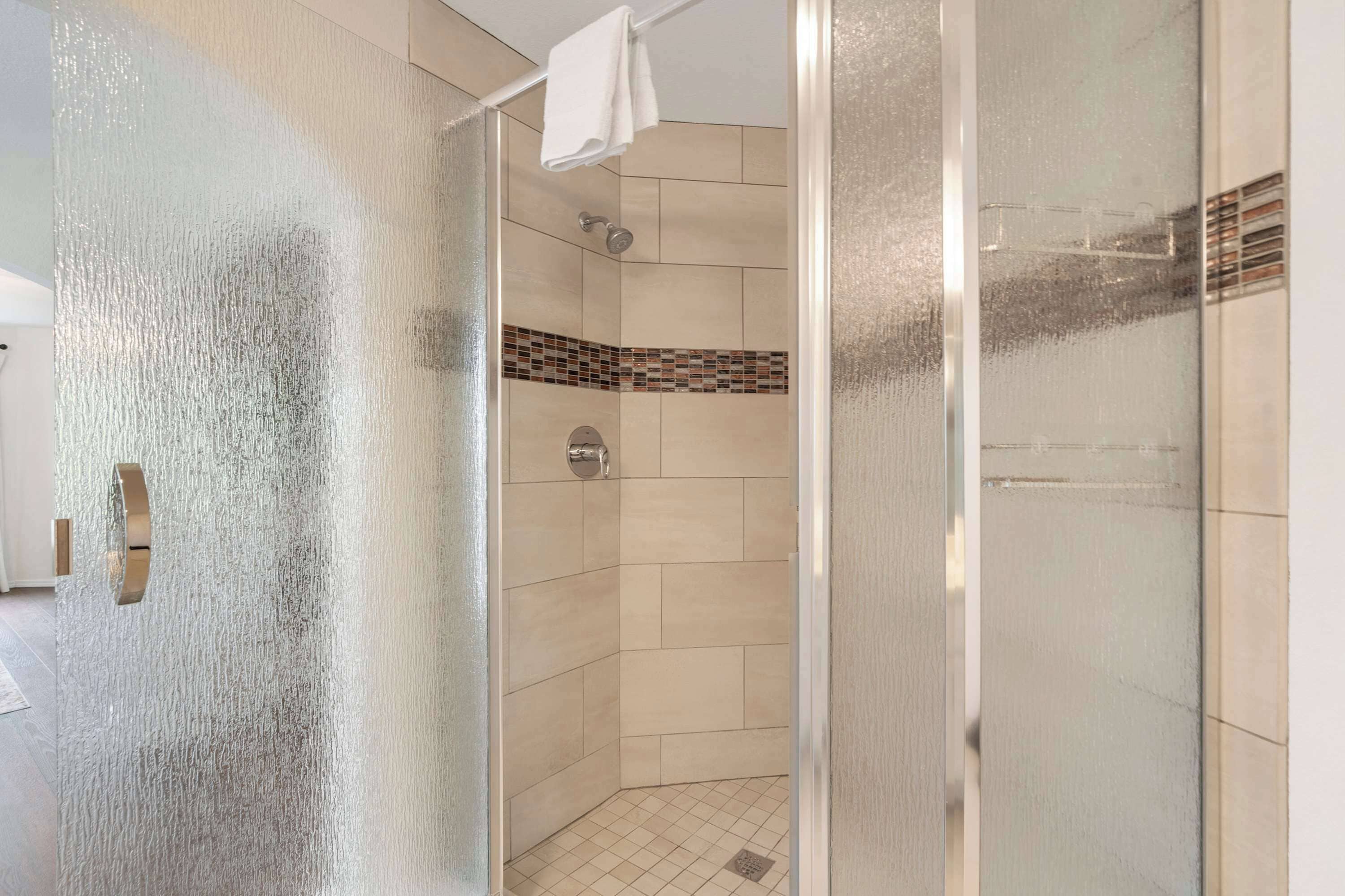A glass-enclosed shower with a tiled floor and a showerhead.