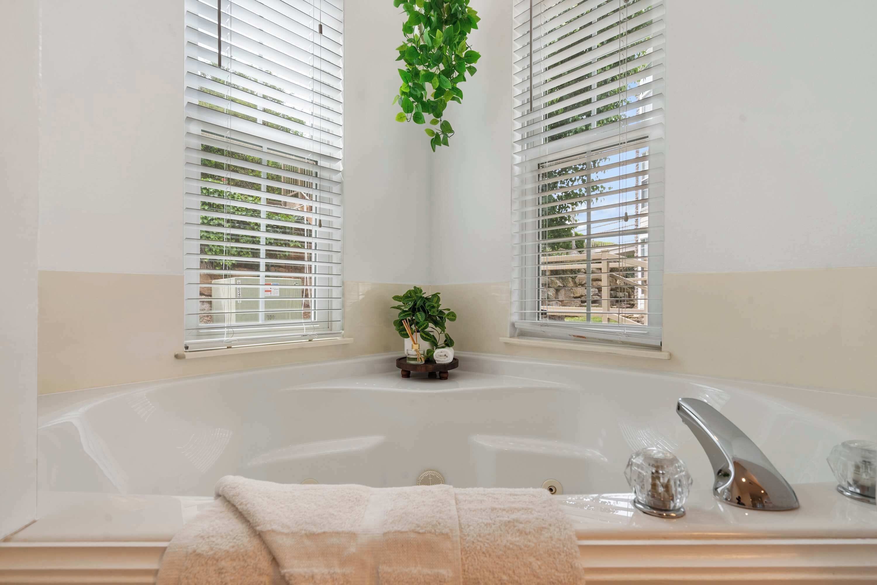Ein Badezimmer mit einer großen Badewanne, zwei Fenstern mit Jalousien und einer hängenden Pflanze.
