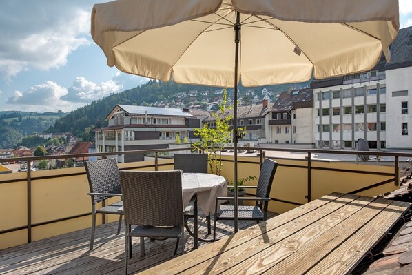 A wooden deck with a table and chairs, an umbrella, and a view of buildings and hills.