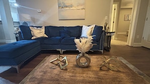 Ein Wohnzimmer mit einem Ecksofa, einem Holztisch und einem Gemälde an der Wand.