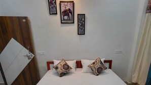 A neatly made bed with patterned pillows, a wooden headboard, and a wall-mounted light fixture. - Majestic Manor (Gorakhpur)