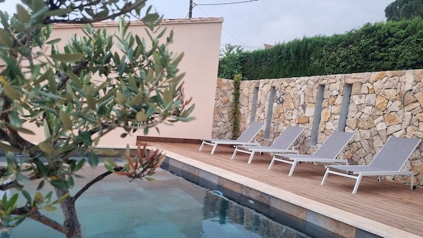A swimming pool with lounge chairs, a stone wall, and a wooden deck. - Villa Mané with swimming pool (Ollioules)