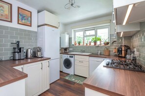 A kitchen with a washing machine, a sink, a stove, and a window with plants.