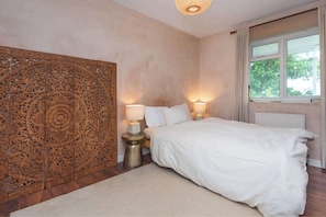 A bedroom with a large bed, two bedside lamps, a decorative wooden panel, and a window with curtains.