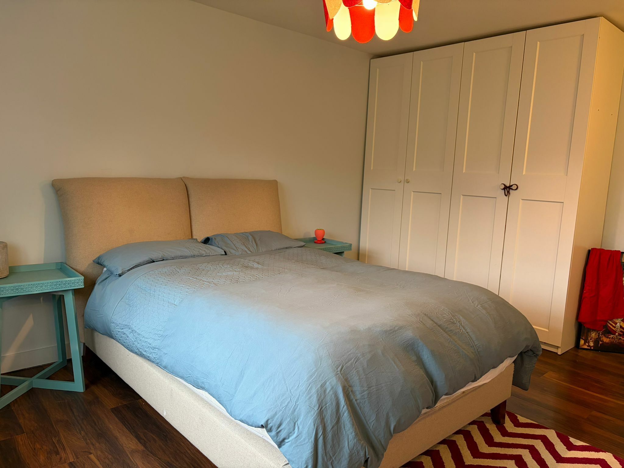 A bedroom with a bed, a nightstand, a wardrobe, and a hanging light fixture.