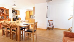 Un comedor amplio con una mesa y sillas de madera, una cocina al fondo y una escalera que sube a otro nivel.
