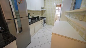 A kitchen with white cabinets, a stainless steel refrigerator, a stove, and a sink. - Apto com Wi-fi Ar-condicionado e Vaga de Garagem (Guarujá)