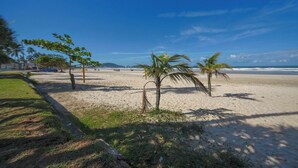 A beach with palm trees, a clear sky, and a distant view of the ocean. - Apto com Wi-fi Ar-condicionado e Vaga de Garagem (Guarujá)