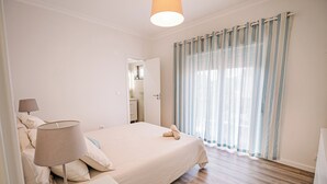 A bedroom with a bed, bedside lamp, and a view of a bathroom through a door. - Close to Lisbon & Beaches (Amora)