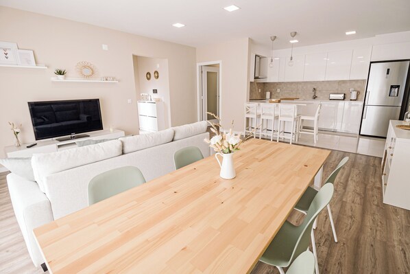 A modern kitchen with white cabinets, a stainless steel refrigerator, and a wooden dining table with chairs.