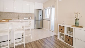 A modern kitchen with white cabinets, a stainless steel refrigerator, and a dining area with white chairs. - Close to Lisbon & Beaches (Amora)