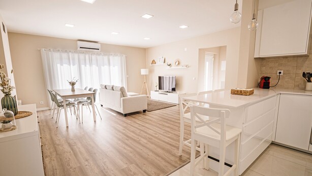 A modern kitchen with white cabinetry, a dining area with a white table and chairs, and a living room with a sofa and a TV. - Close to Lisbon & Beaches (Amora)