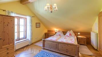 A bedroom with a wooden bed, a window with curtains, a chandelier, and a radiator.