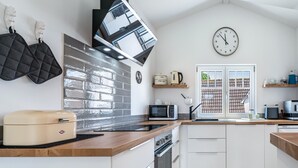 Una cocina moderna con microondas, tostadora y hervidor sobre la encimera, un reloj en la pared y una ventana con vistas a un edificio.