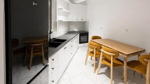 A modern kitchen with white cabinets, a black refrigerator, and a wooden dining table with yellow chairs. - Sasori Apartments (Sarande)