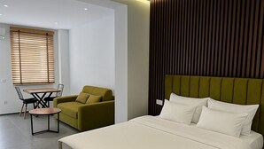 A modern bedroom with a large bed, a green sofa, and a dining area with a table and chairs. - Sasori Apartments (Sarande)