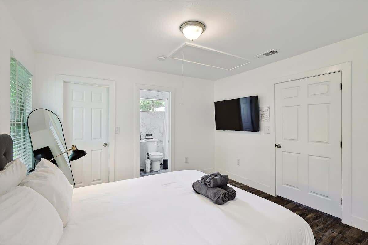 A hotel room with a bed, a TV mounted on the wall, and a bathroom visible through an open door.