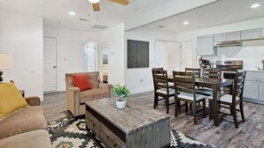 A spacious living room with a wooden coffee table, a sofa, and a dining area with wooden chairs. - Serene Escape - Peaceful 3-BD Retreat with Yard (Grand Prairie)