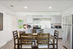 A modern kitchen with white cabinets, stainless steel appliances, and a dining area with wooden chairs.