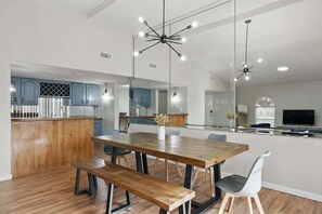 A modern kitchen with wooden cabinets, a dining table with benches, and a large mirror reflecting the space. - Luxury Retreat in Carrollton - Pool, Patio & More (Carrollton)