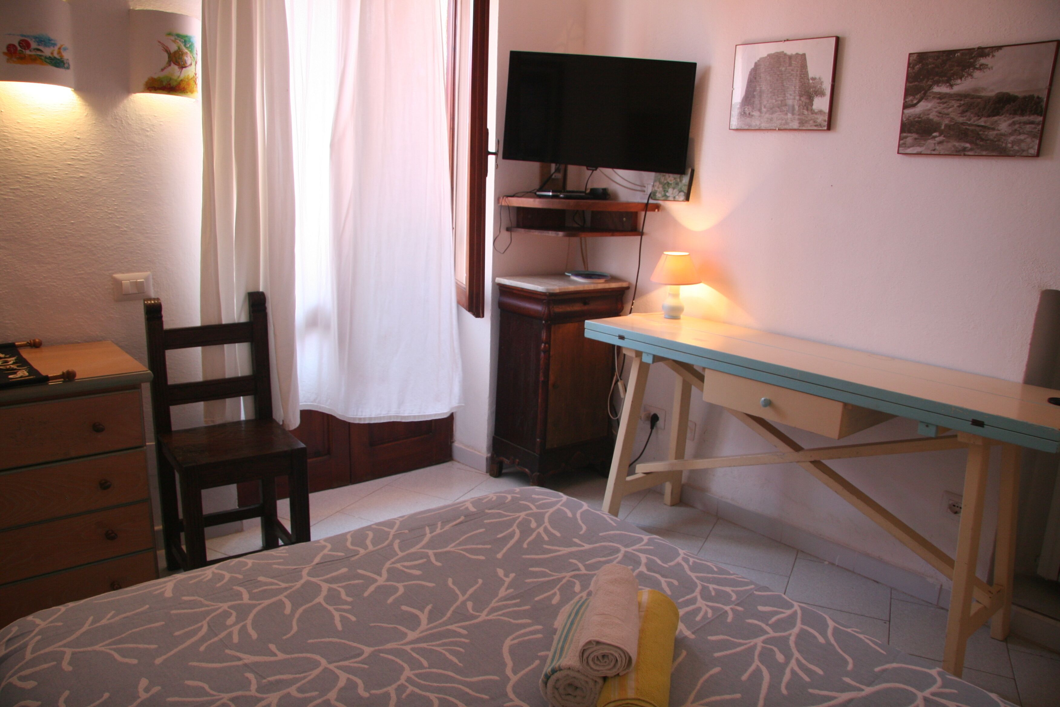 Ein Schlafzimmer mit Bett, Schreibtisch, Stuhl, Fernseher und Lampe.