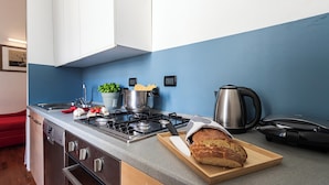 Una cocina moderna con estufa a gas, hervidor y hogaza de pan sobre tabla de cortar.