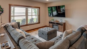 A spacious living room with a large window, a flat-screen TV, and a cozy seating area. - The Lakeside On North Long (Merrifield)