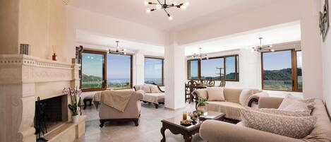 A spacious living room with a fireplace, two sofas, a coffee table, and large windows offering a view of the landscape.