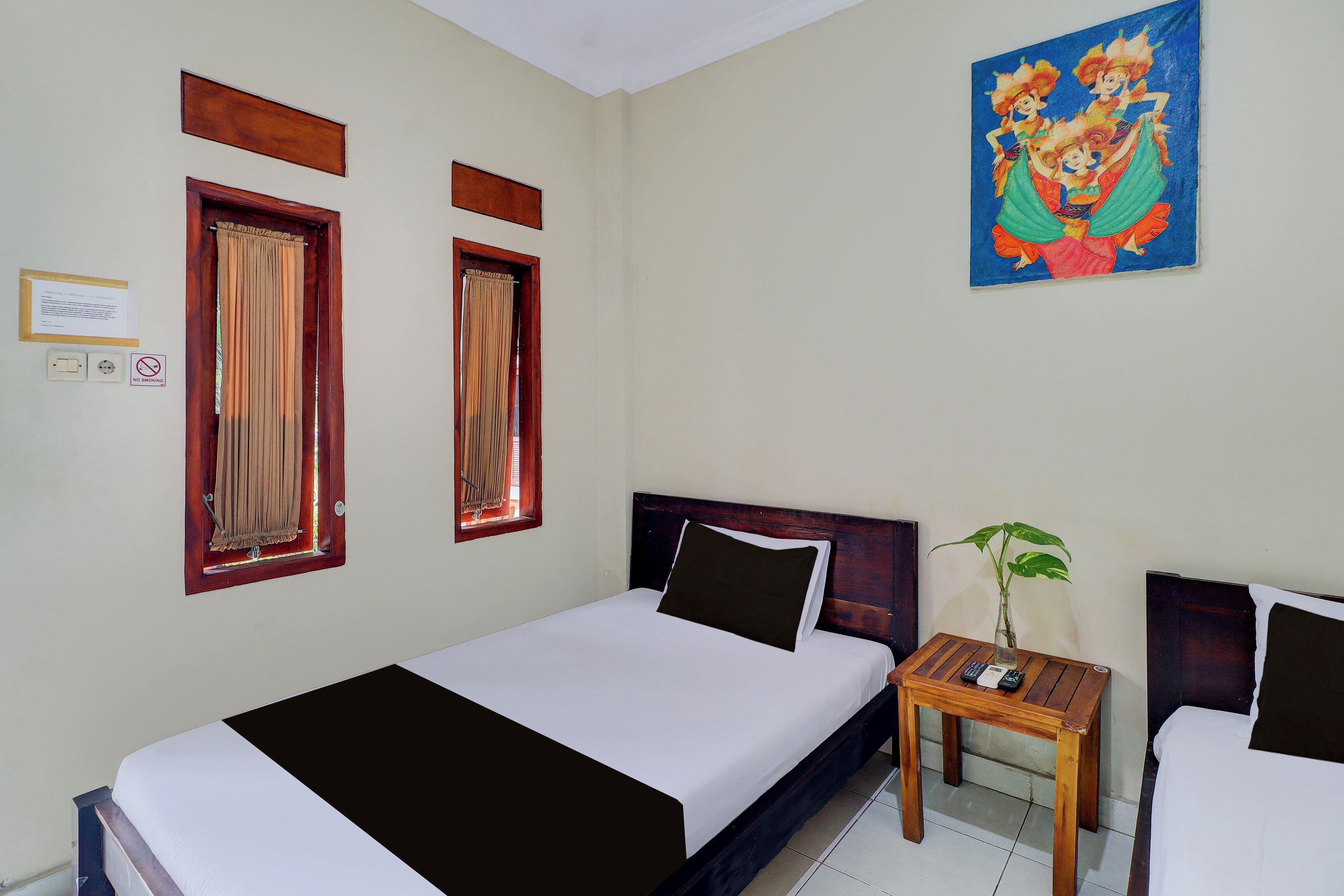 A hotel room with a bed, a small table with a plant, and a painting on the wall.