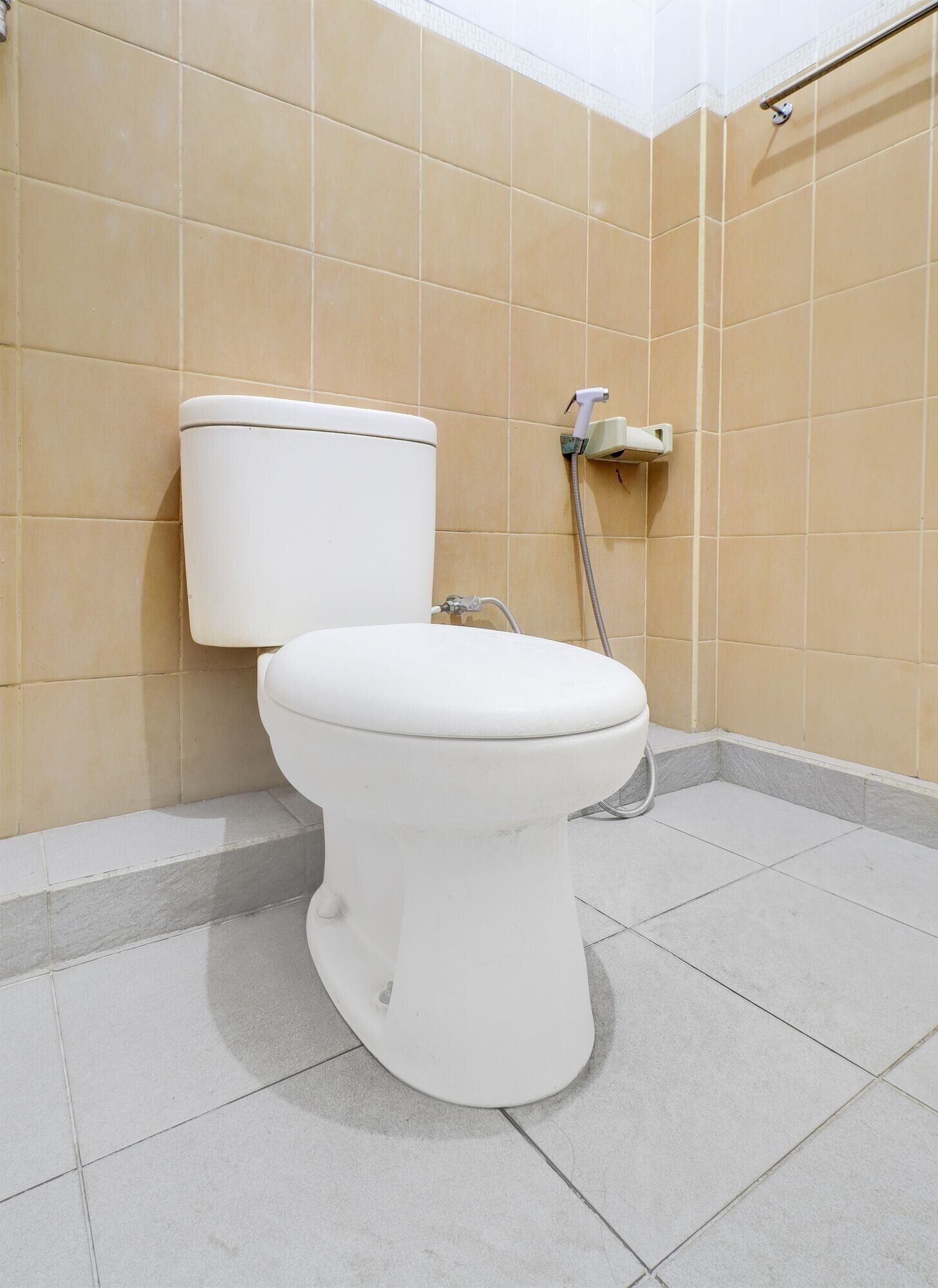 A toilet in a bathroom with beige tiles on the walls and a white floor.