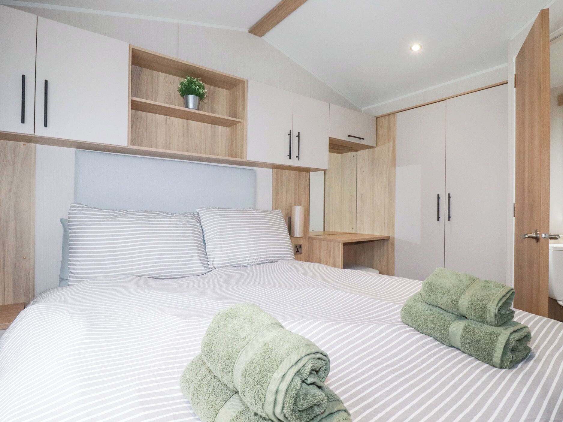 Une chambre à coucher avec un lit, une literie à rayures, une petite étagère avec une plante et une armoire en bois.
