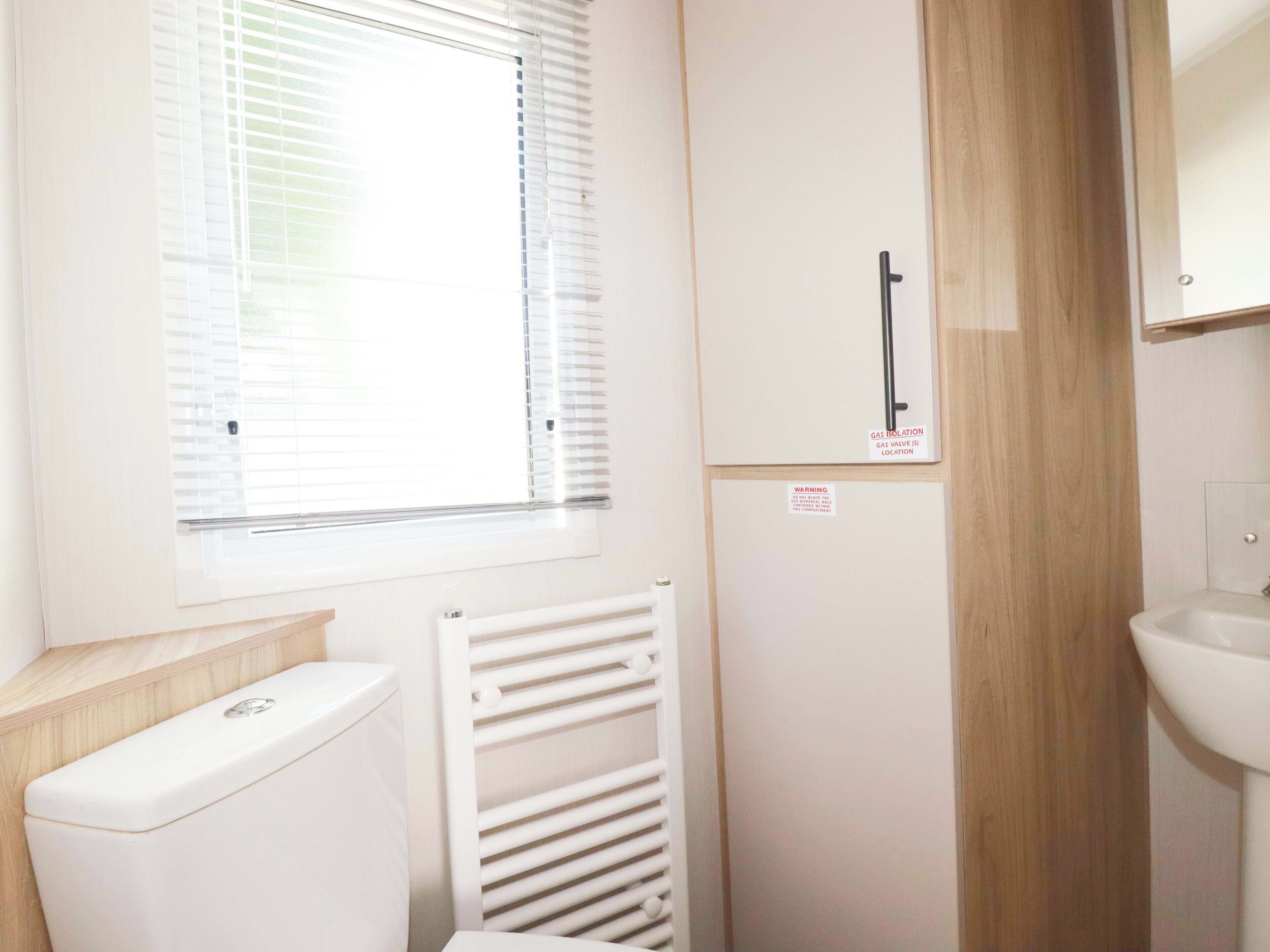 A bathroom with a toilet, a radiator, a window with blinds, and a sink.