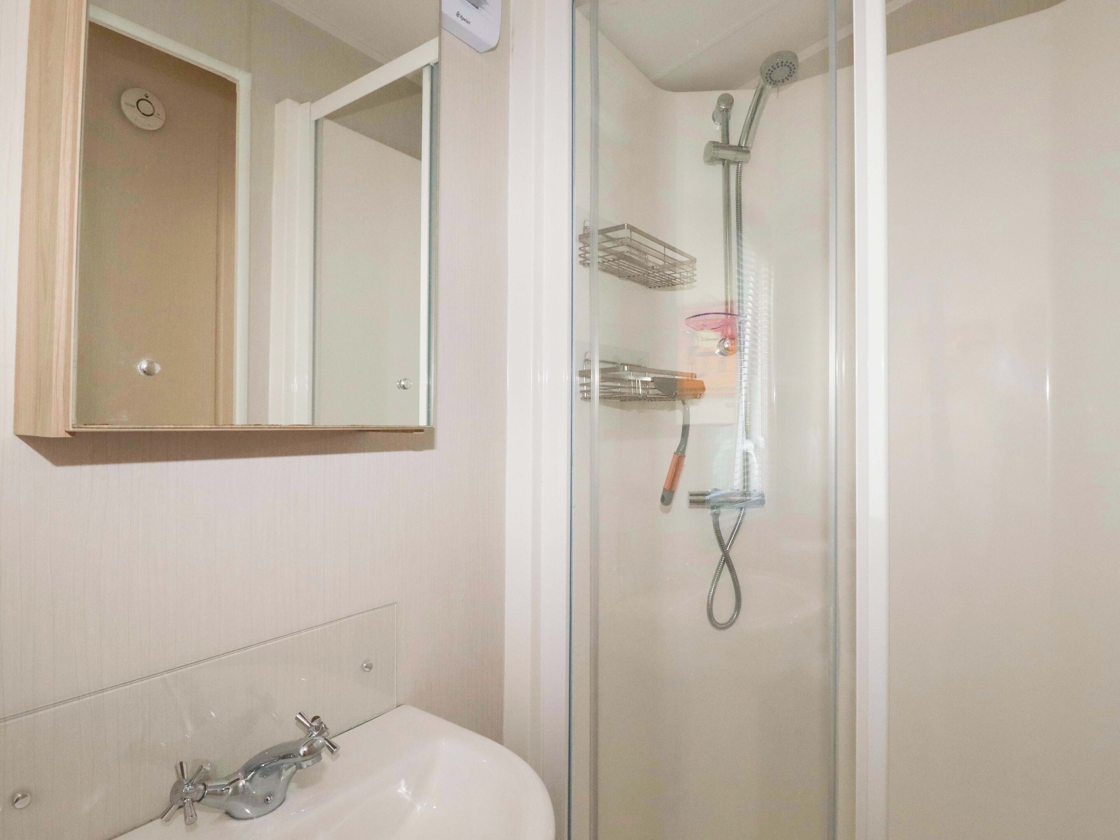 A bathroom with a glass-enclosed shower, a sink with a faucet, and a mirror above the sink.