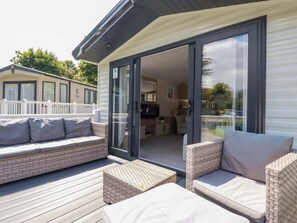 Un espace extérieur aménagé, abrité et doté de meubles en osier, avec une porte en verre donnant accès à un espace intérieur.