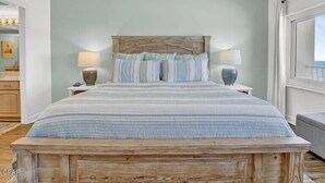 A bedroom with a wooden headboard, a bed with striped bedding, two bedside lamps, and a view of the outdoors through a window. - Coral Reef Unit #1304 (Beachfront 2 bedroom 2 bath condo on the 13th floor) (Panama City Beach)