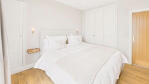 A bedroom with a large bed, white walls, wooden flooring, and a wooden door.