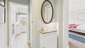 A hotel room with a bathroom, a bed, a bedside table with a lamp, and a mirror on the wall. - Host & Stay | Bell Cottage (Kirknewton)