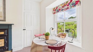 A dining area with a round table, red chairs, a small potted plant, and a window with a floral valance. - Host & Stay | Bell Cottage (Kirknewton)